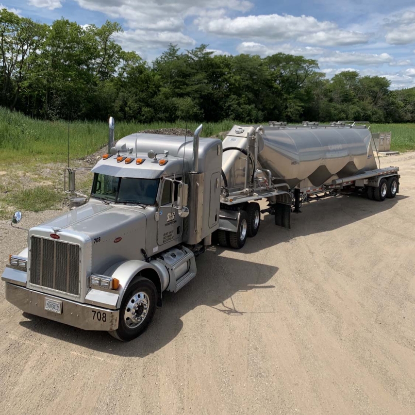 Large grey 18 wheeler parked on sand.