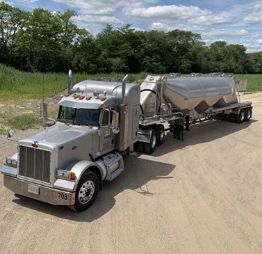 A large grey 18 wheeler parked on sand.